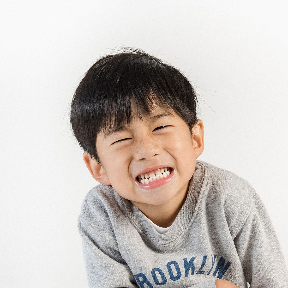 A smiling boy with short black hair in a light blue t-shirt against a white studio background