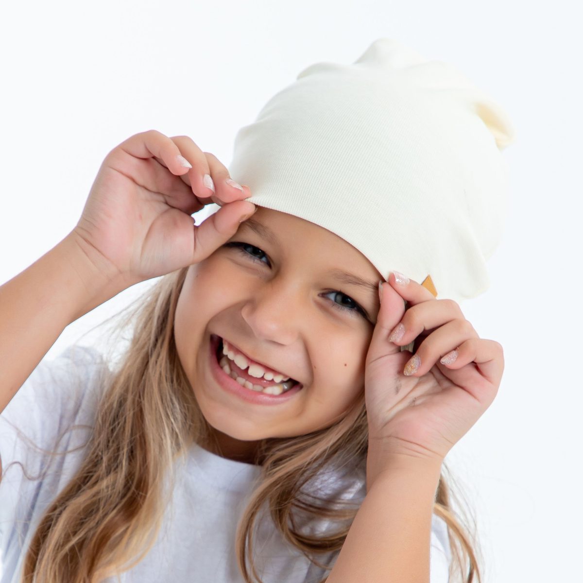 A smiling girl in a white beanie and white t-shirt against a white studio background