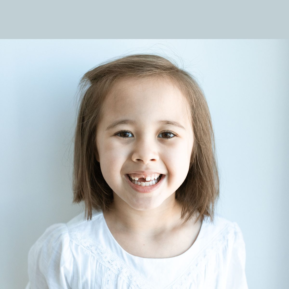 A smiling girl with two puffs of hair in a white top against a light studio background
