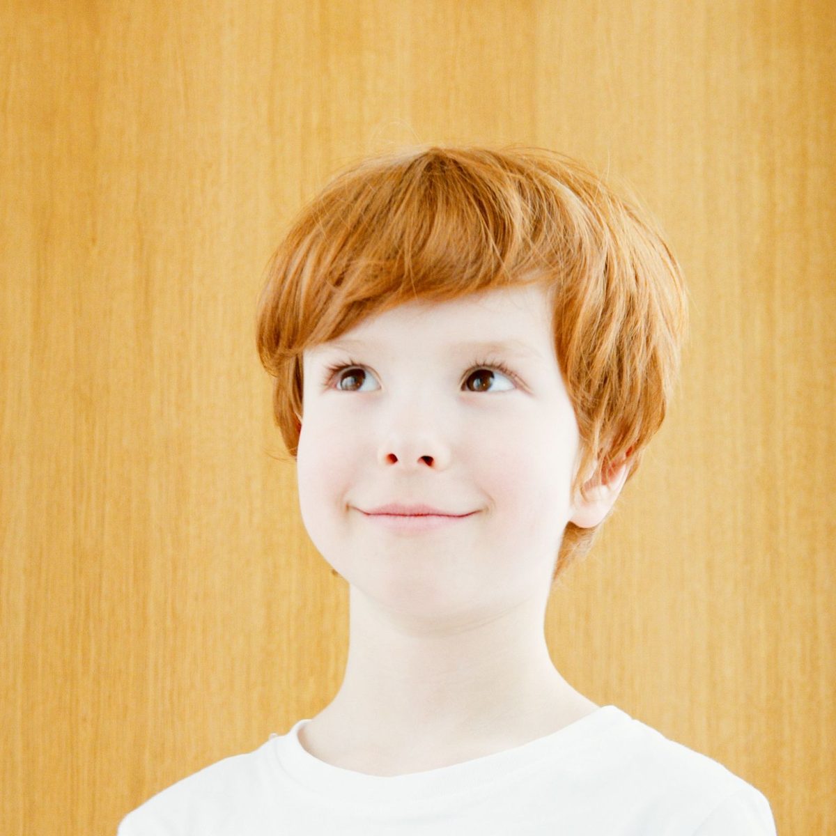 A smiling boy with short red hair in a red t-shirt against a light studio background